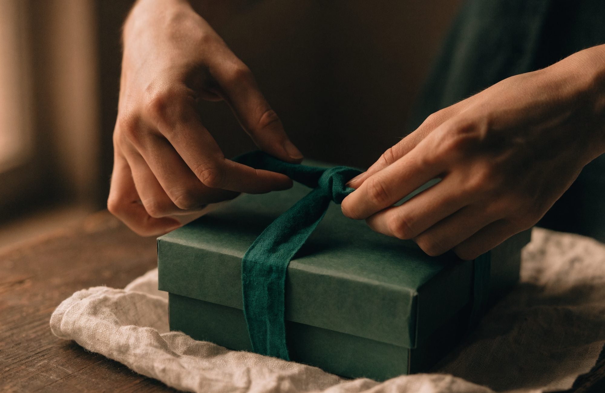 Dos manos atando una cinta de tela sobre una caja de regalo
